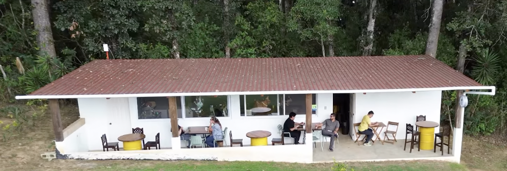 Nuevo local de Chucho Perdido: fachada blanca, techo rojizo y mesas junto a los árboles.